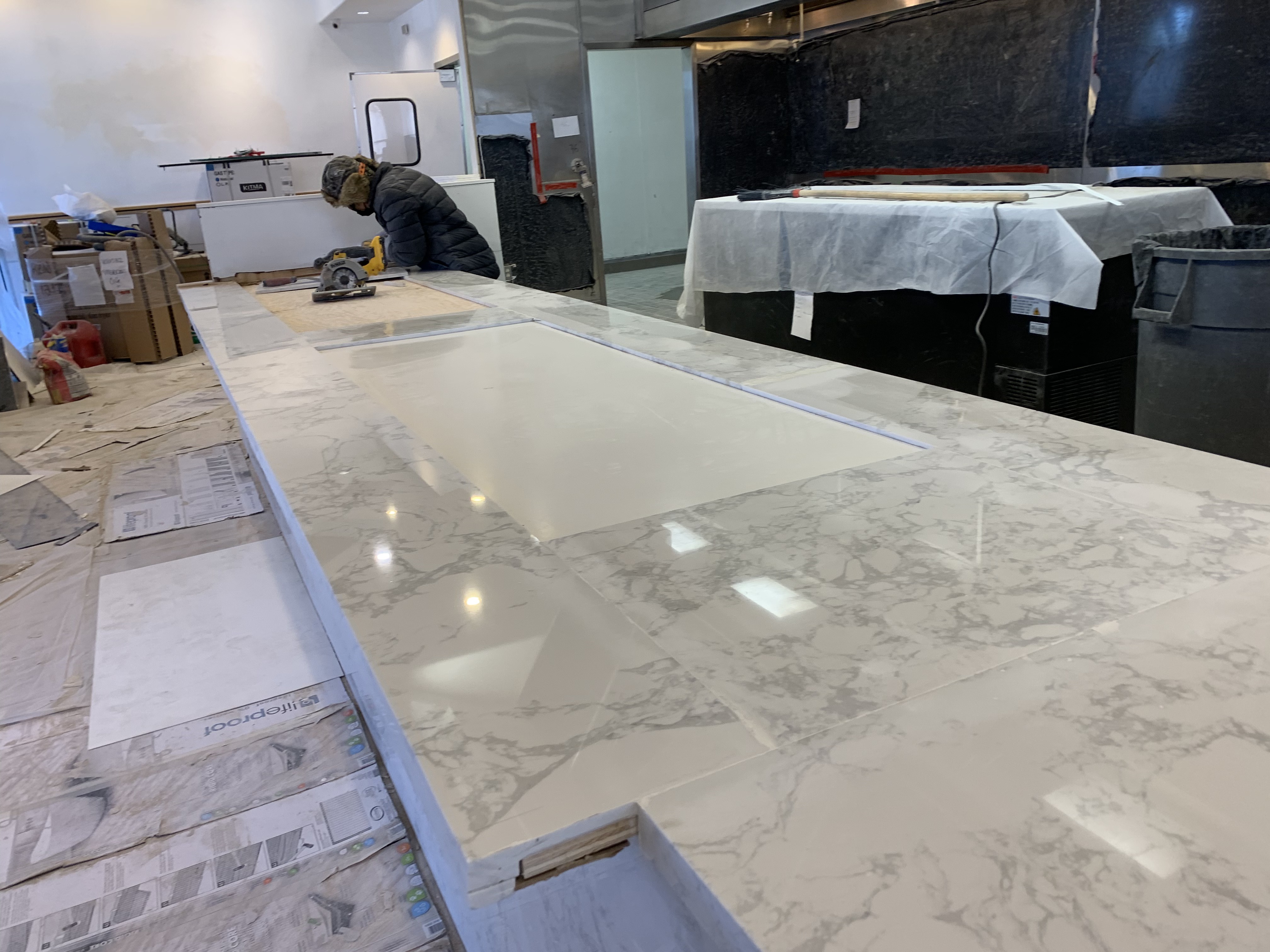 Worker cutting a quartz bar top to fit with a circular saw in a commercial kitchen