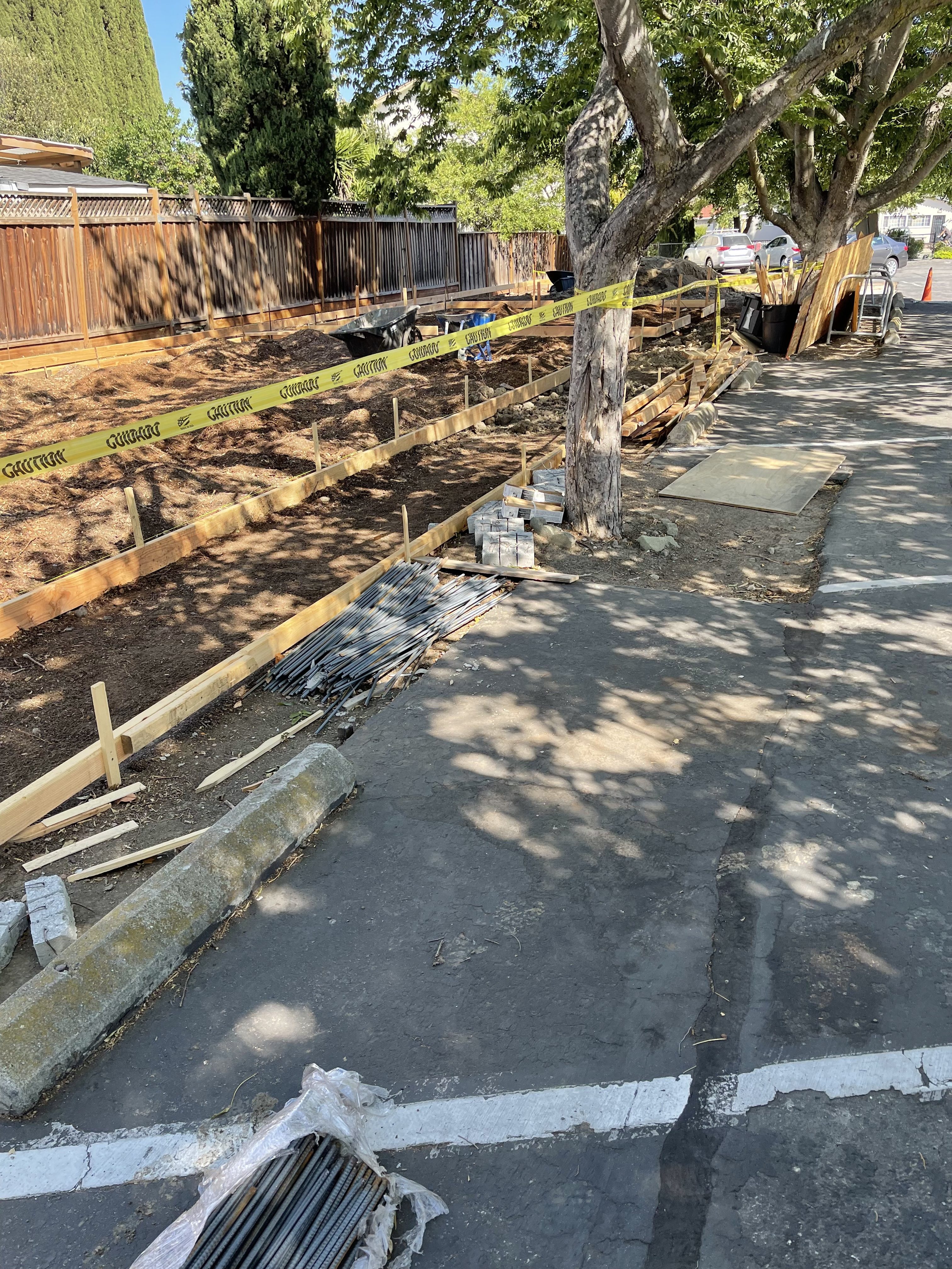 Wood foundation forms set along a fence line with caution tape and rebar stacked nearby