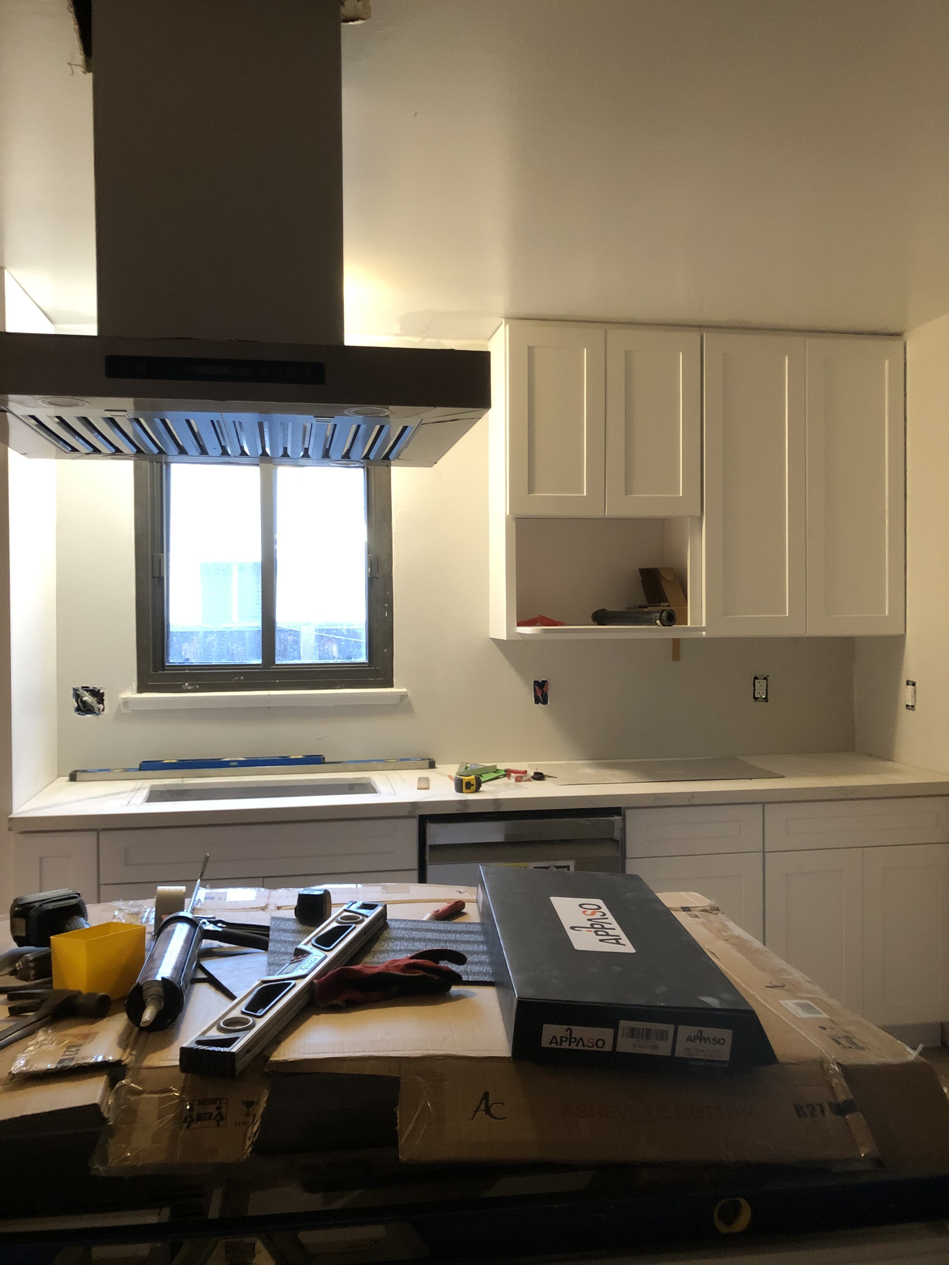White kitchen cabinets and island range hood installed with the countertop still being fitted